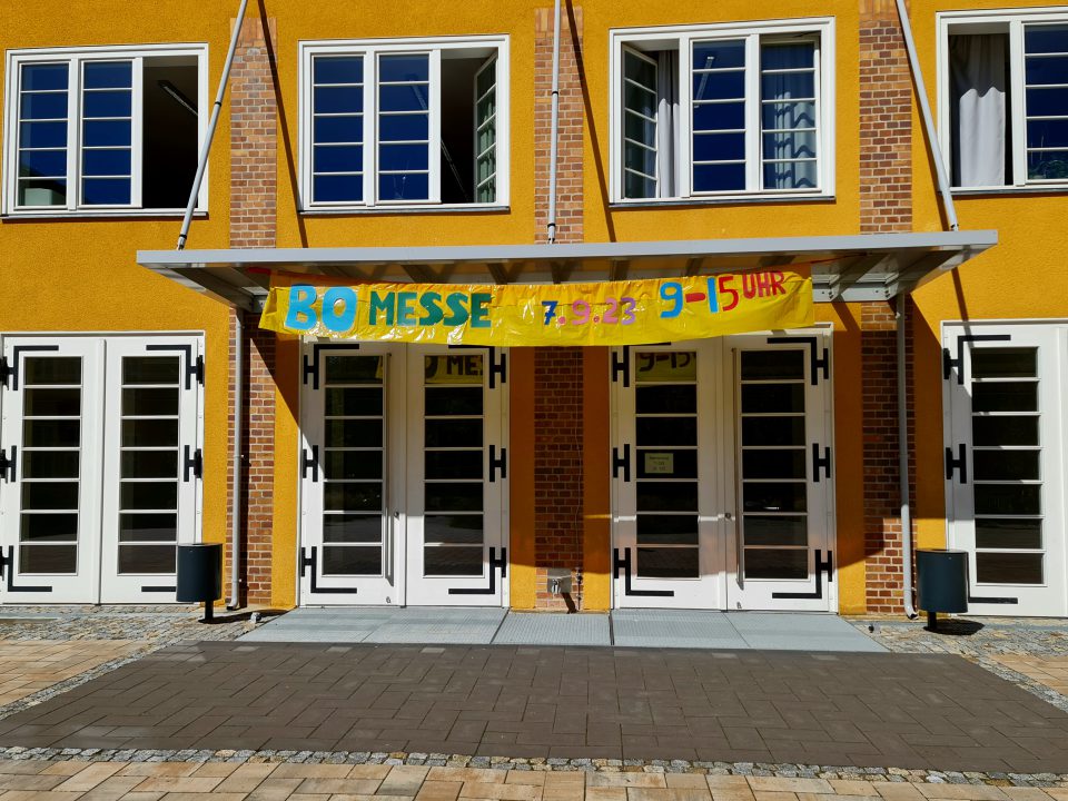 Foto der Eingangstür der Schule mit dem Messebanner